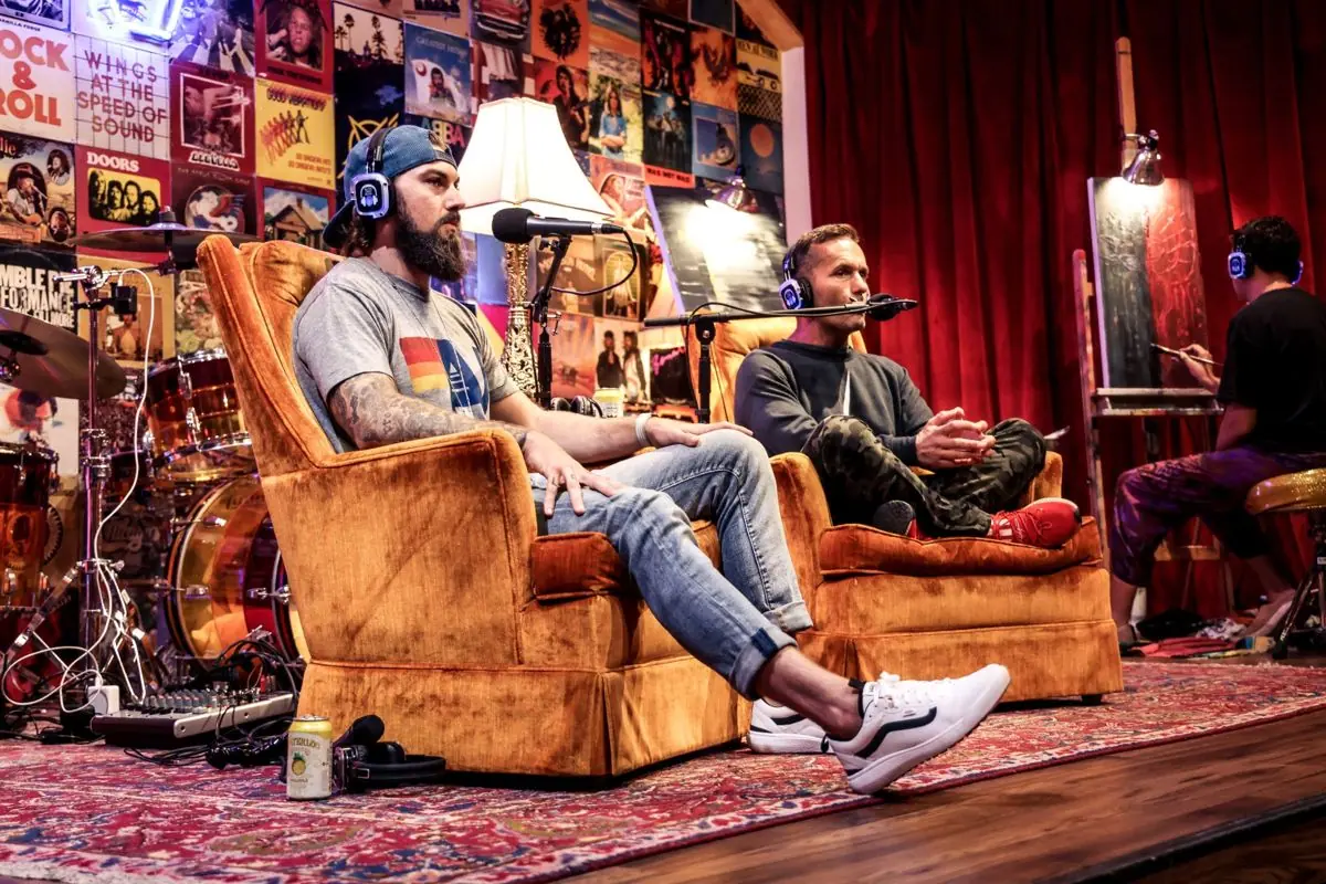 Two hosts in armchairs on stage, mics up