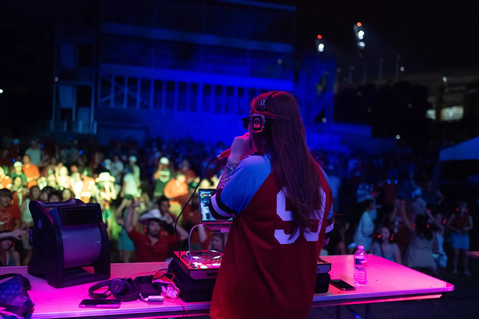DJ at the booth with the festival crowd dancing below in blue light