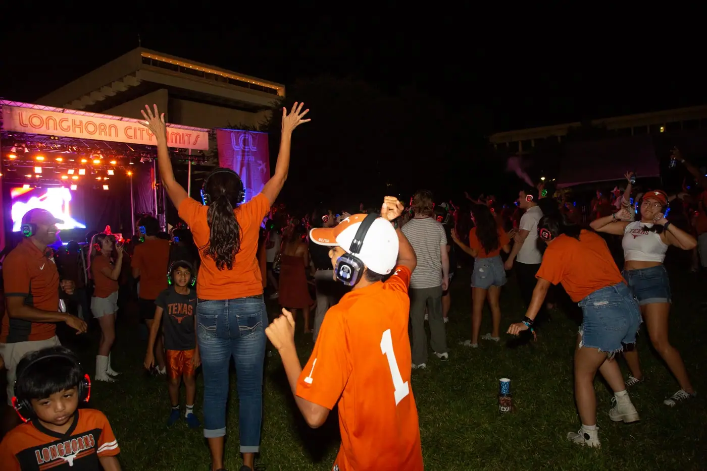 Families and students dancing on the lawn, hands up, headphones on