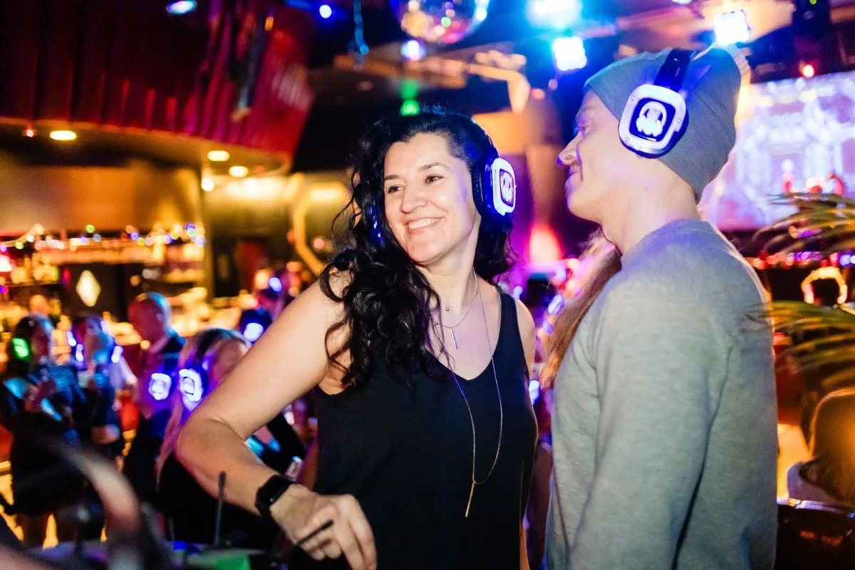 A guest laughing mid-dance beside her partner, headphones on
