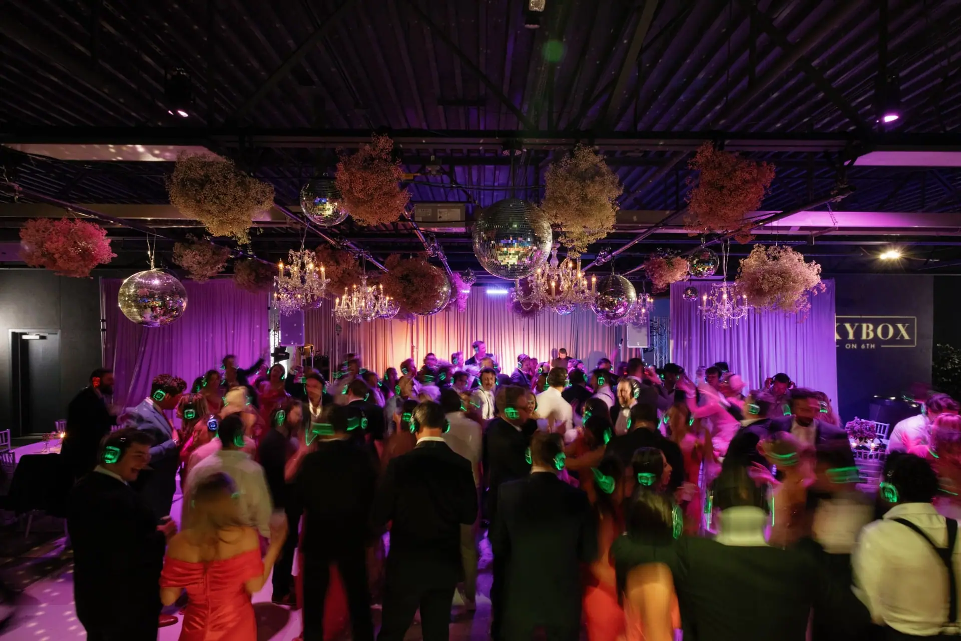 Reception dance floor under chandeliers and disco balls, guests in glowing headphones
