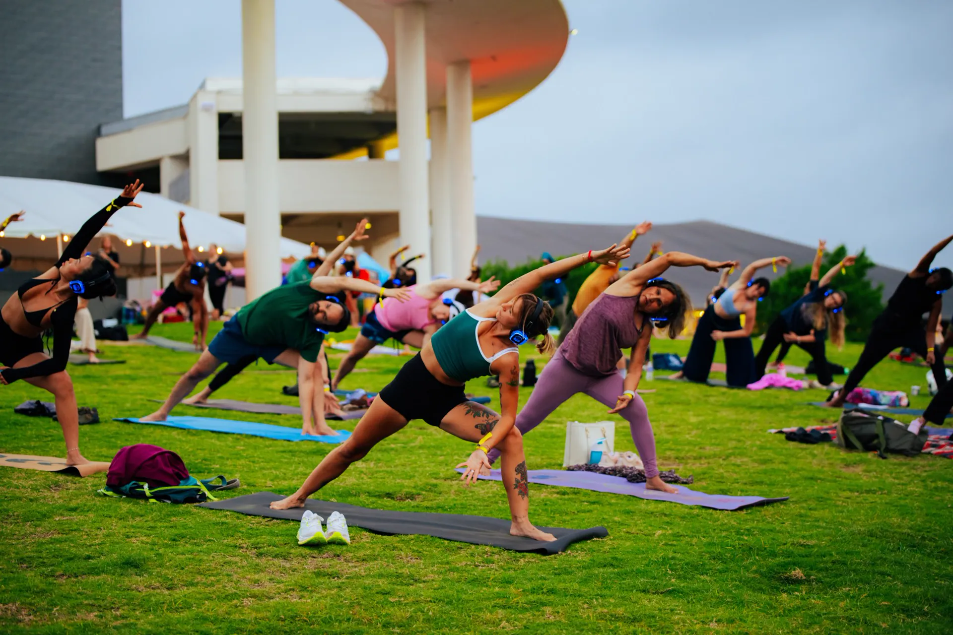 A yoga class on a green lawn, everyone stretching with headphones on