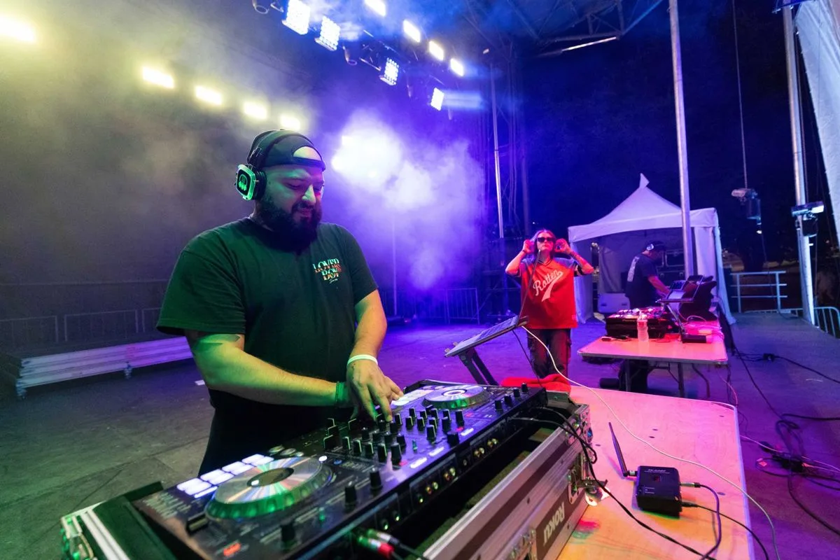 A DJ in a cap behind the decks, purple stage light