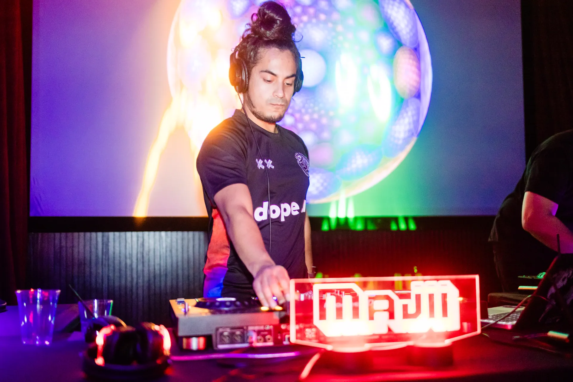 A DJ at the decks in front of a glowing projection