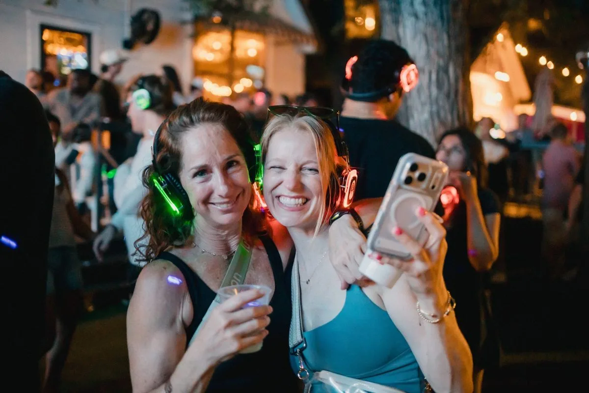 Two friends beaming at the camera, headphones glowing