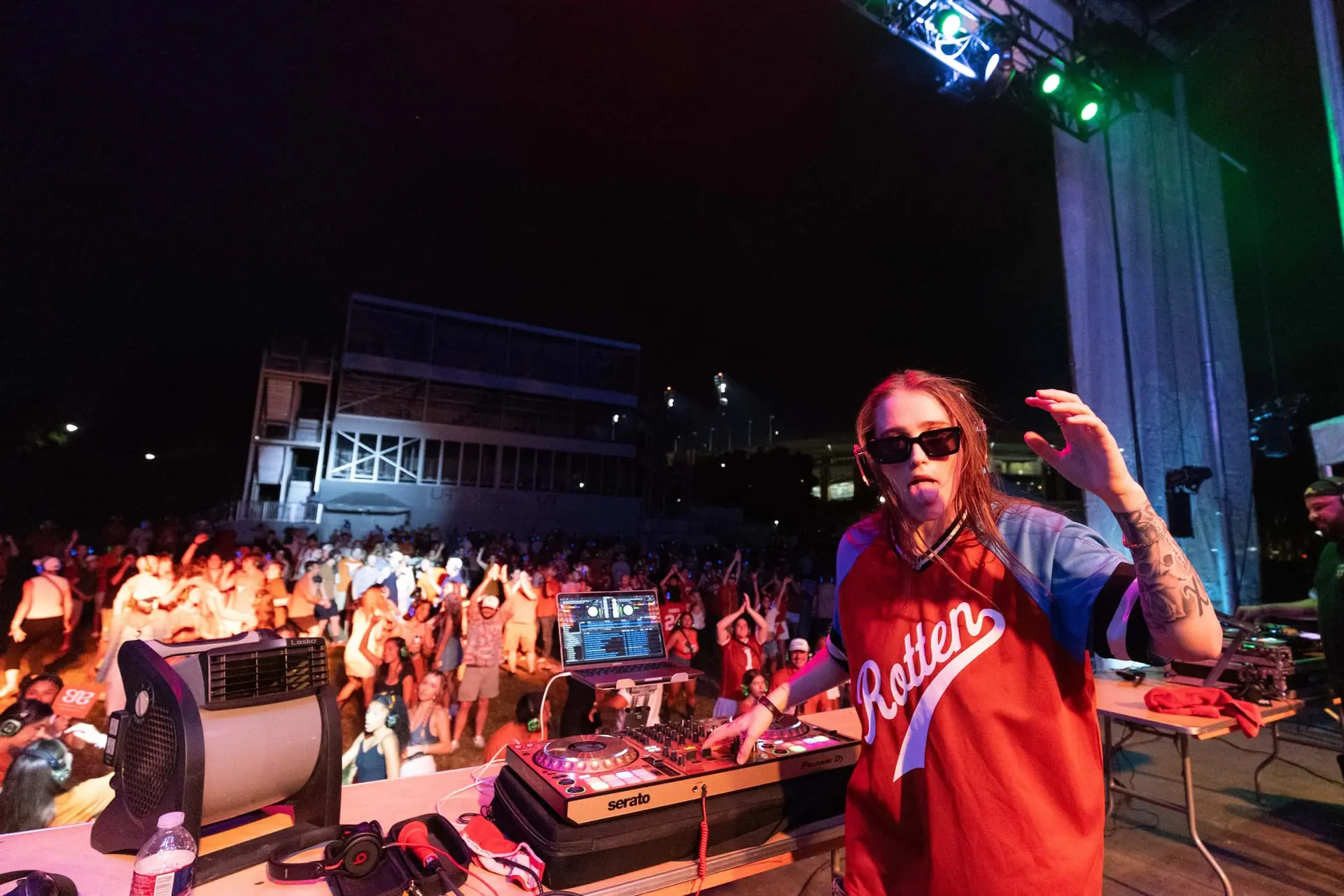DJ in a red jersey at the booth, crowd dancing below the stage