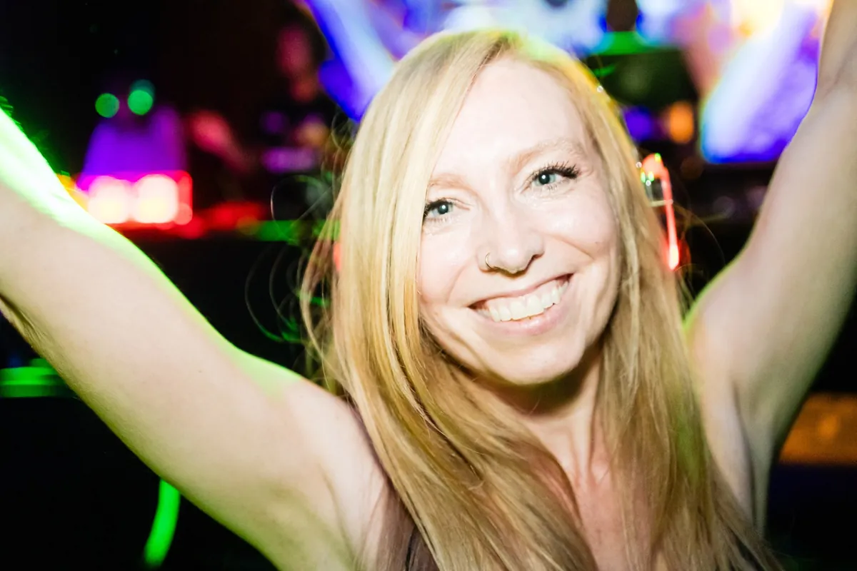 A guest dancing with her arms up, headphones glowing under club lights