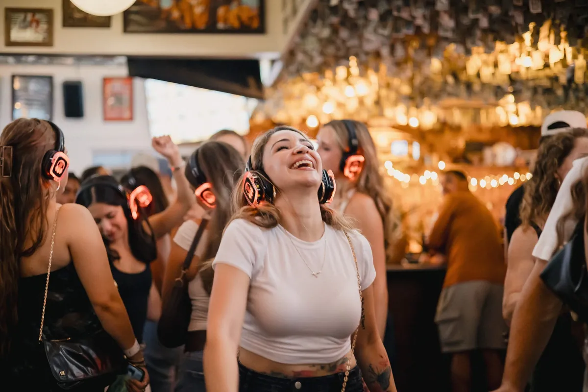 A guest laughing mid-dance in a packed bar, glowing headphones all around